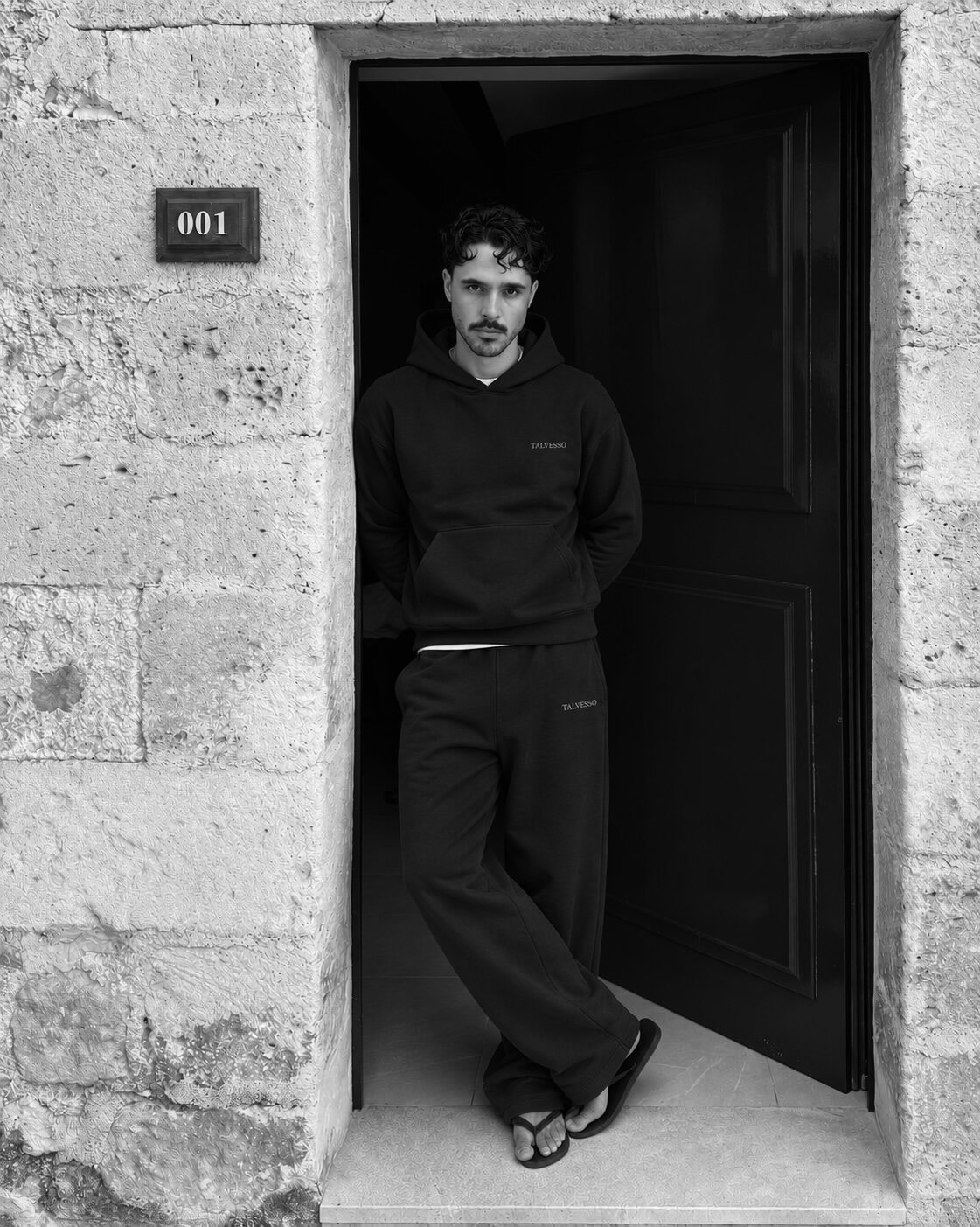 Male model in the navy TALVESSO tracksuit standing in a stone doorway